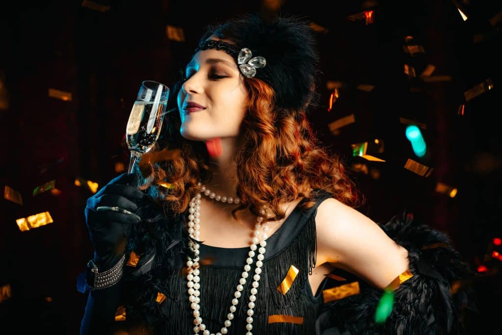 Woman dressed in Great Gatsby era dancing under confetti rain on velours background for an event at a medi spa in Calgary.